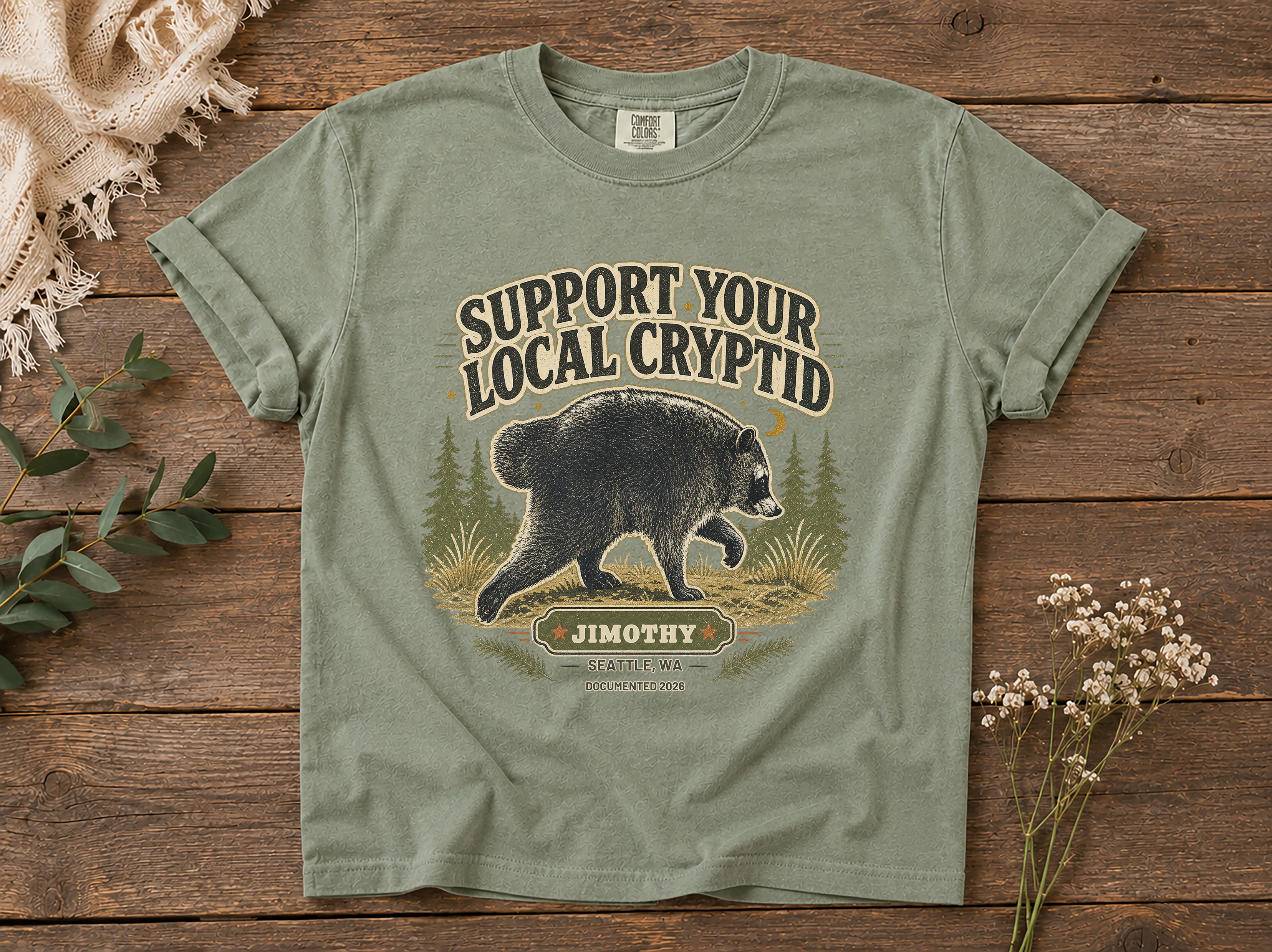 Featured muted green raccoon cryptid t-shirt mockup with a vintage-style front graphic.